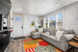 A cozy living room with a grey sectional sofa, a colorful rug, and a white door with a window. - The Grey Pearl: Cozy Coastal Retreat (Dennis Port)