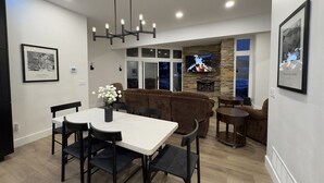 A modern living room with a white dining table, black chairs, a brown sofa, and a stone fireplace. - Modern Luxury 3BR Condo Steps Away from Deer Valley Resort w/ Hot Tub, Fireplace (Park City)