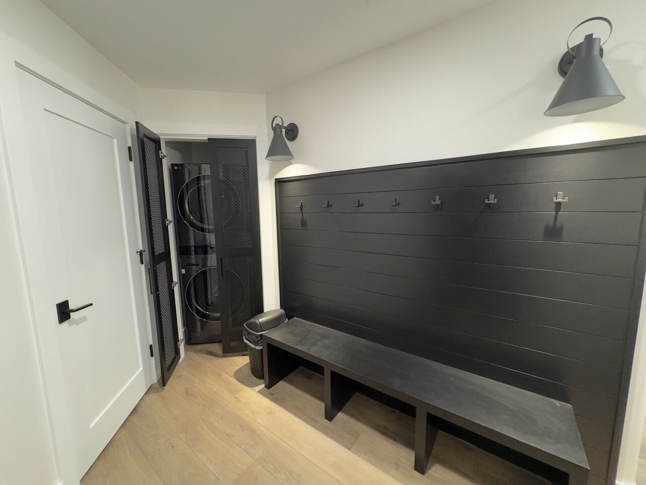 Un couloir avec un banc, un porte-manteau et une porte donnant sur une pièce dont un mur est noir et qui possède une fenêtre circulaire.