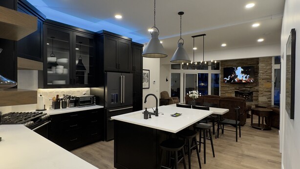A modern kitchen with dark cabinetry, a central island, and a dining area with bar stools. - Modern Luxury 3BR Condo Steps Away from Deer Valley Resort w/ Hot Tub, Fireplace (Park City)