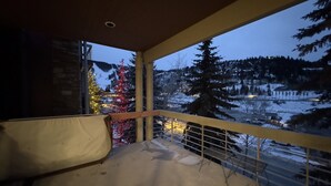 A balcony with a view of a snowy landscape and a decorated Christmas tree. - Modern Luxury 3BR Condo Steps Away from Deer Valley Resort w/ Hot Tub, Fireplace (Park City)