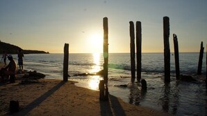 Une plage avec des poteaux en bois et des personnes près de l’eau au coucher du soleil.