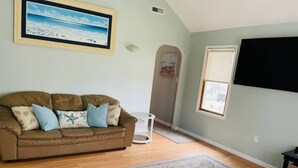 A living room with a brown leather couch, a white coffee table, a framed picture of a beach, and a large window.