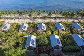 A resort with multiple bungalow-style accommodations, each with a sloped roof and solar panels, surrounded by lush greenery and palm trees, overlooking a sandy beach. - Mai Sunset Beach Resort (Naviti Island)