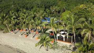 A beach resort with palm trees, a pool, and outdoor seating.