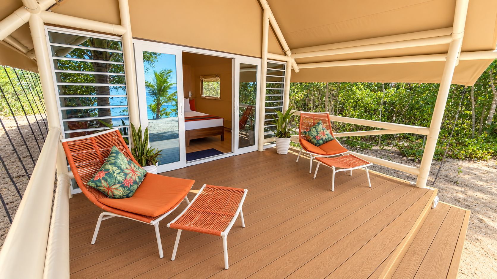 A covered outdoor area with two wicker chairs and a small table, a sliding glass door leading to a room, and a view of the beach.