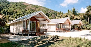 Two bungalow-style accommodations with wooden decks and large windows, set against a backdrop of lush greenery and a mountain. - Mai Sunset Beach Resort (Naviti Island)