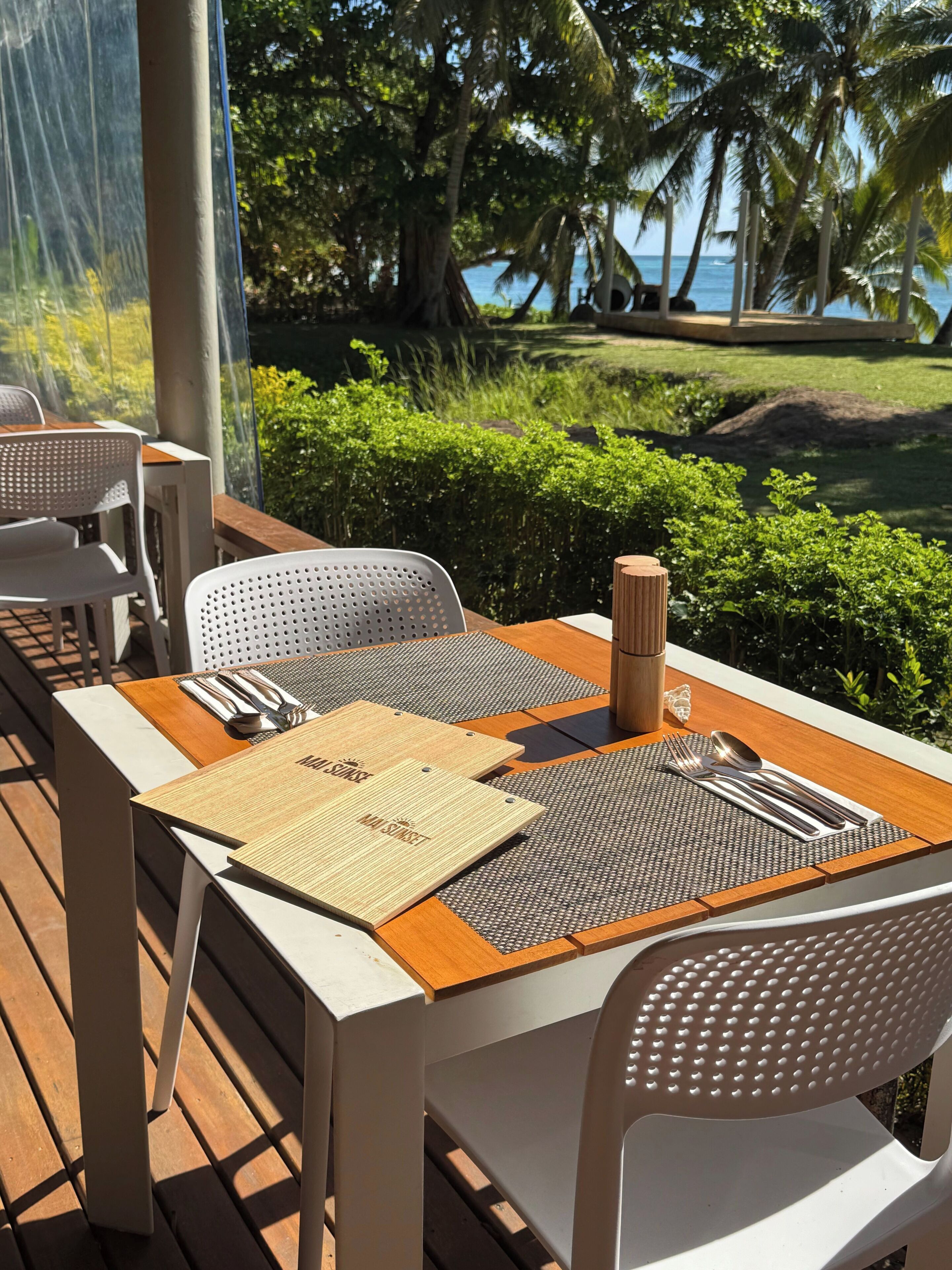 An outdoor dining area with tables and chairs, a wooden table, a woven placemat, cutlery, and a candle holder.