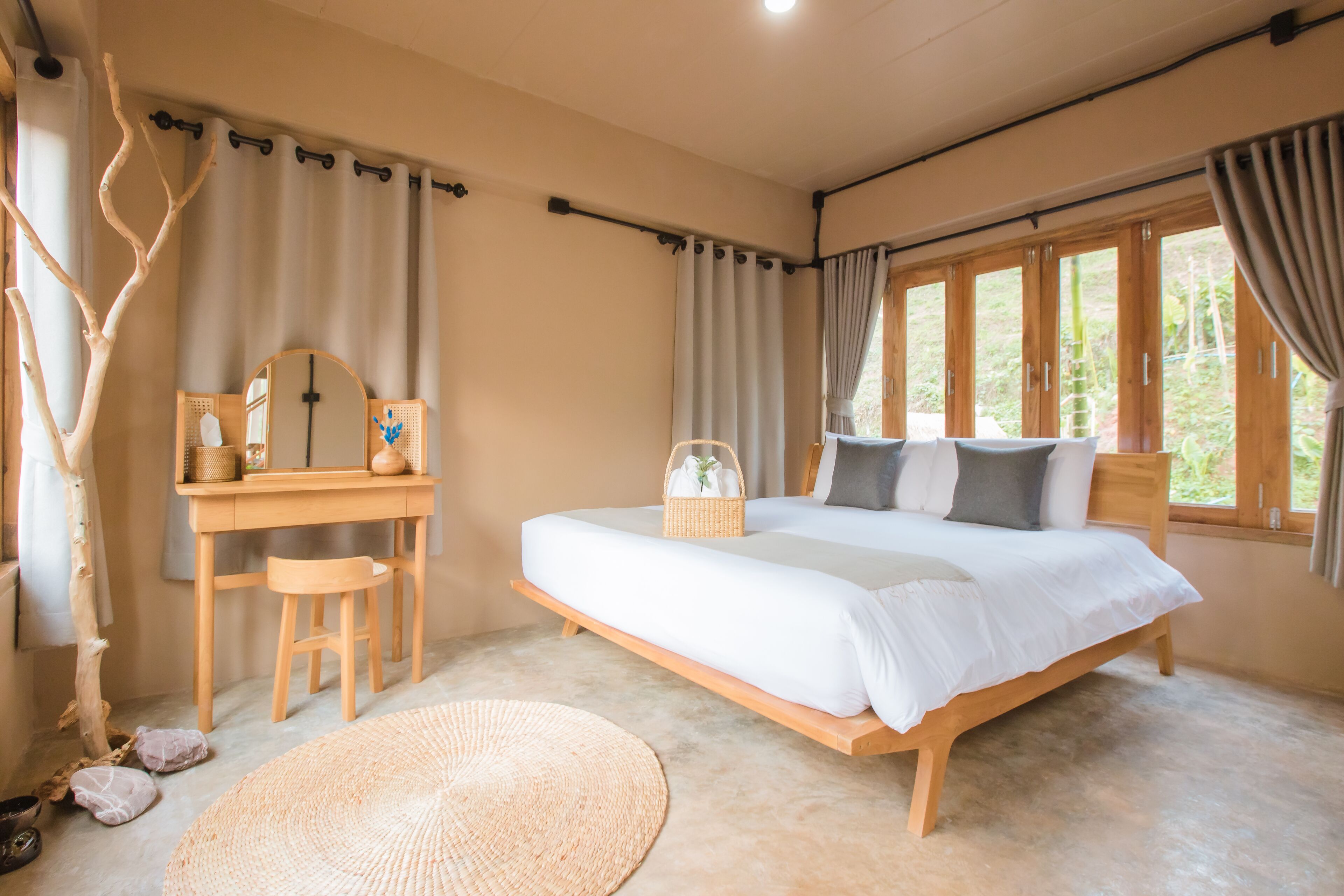A bedroom with a wooden bed, a desk with a chair, a round woven rug, and a window with curtains.