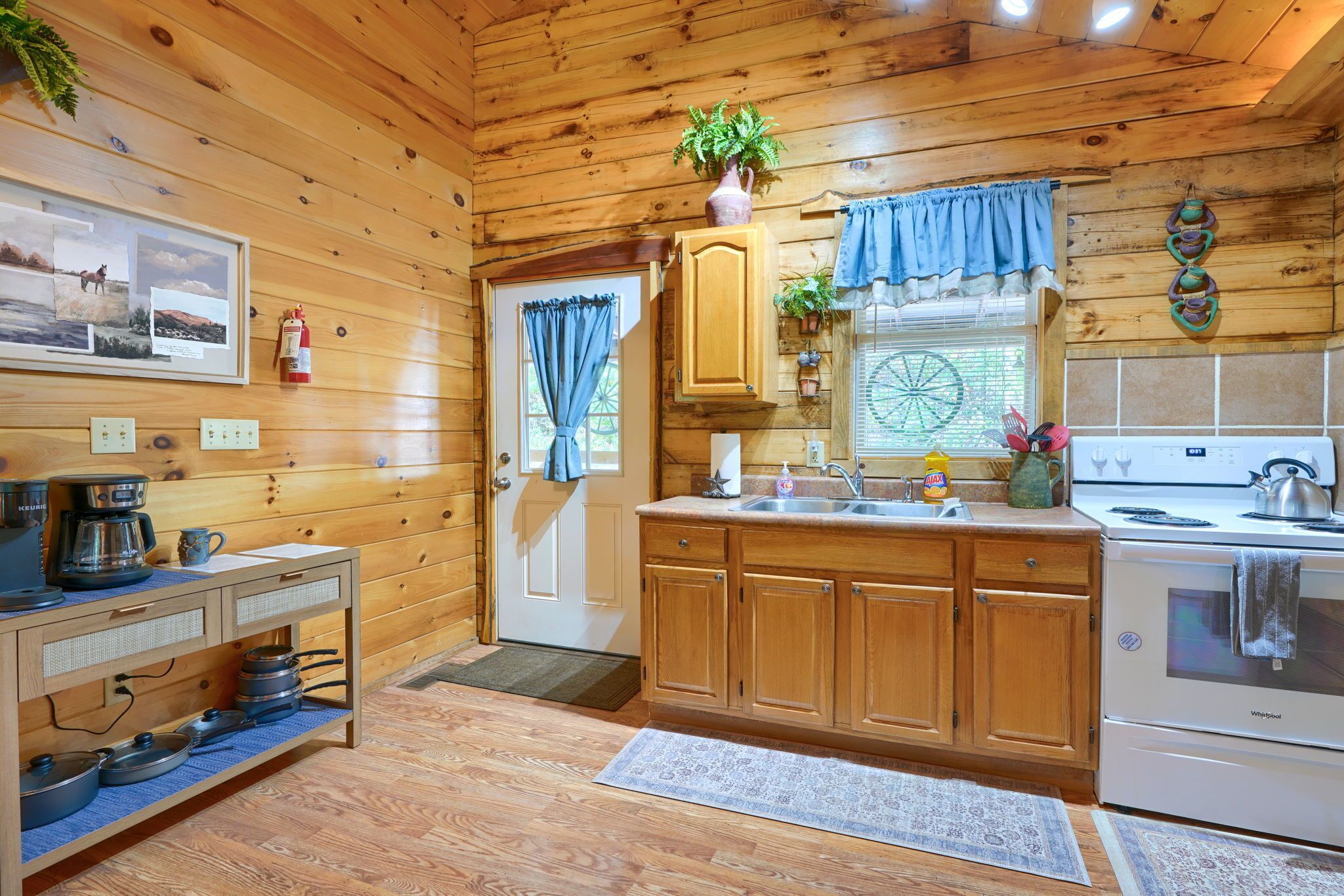 Interior de una cabaña de madera con kitchenette, armarios de madera, estufa y cafetera.