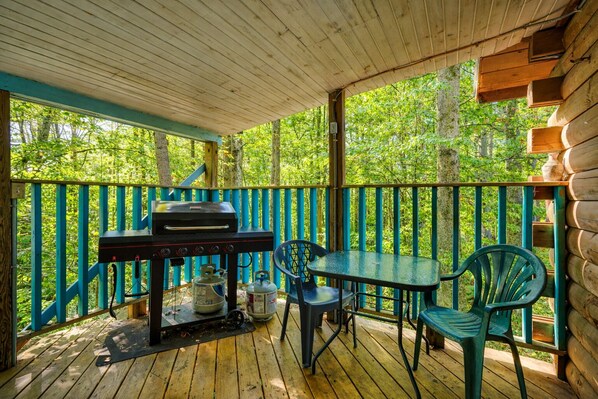 Una terraza exterior de madera con una parrilla, sillas y una mesa.