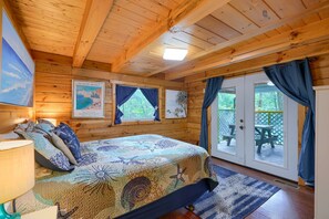 L’intérieur d’un chalet en bois, avec un lit, un tableau et une vue à travers la porte.