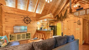 A cozy cabin interior with a wooden interior, a television, a sofa, and a kitchen area.