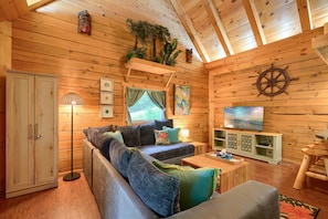 L’intérieur d’un chalet accueillant, avec un plafond en bois, un canapé, un téléviseur et un meuble.