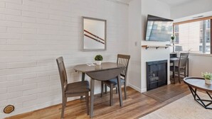 A dining area with a round table, two chairs, a small potted plant, a fireplace, and a mounted television. - Prospector Place - 2(King)Bed 2Bath - Easy to ski! (Park City)