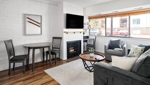 A living room with a fireplace, a television, a dining table with chairs, and a sofa. - Prospector Place - 2(King)Bed 2Bath - Easy to ski! (Park City)