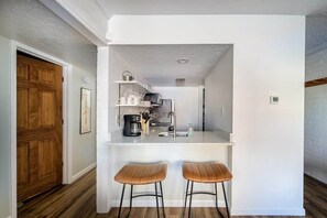 Una cocina moderna con encimera blanca, dos taburetes y una puerta de madera.