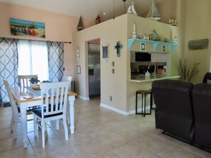 A dining area with a table and chairs, a kitchen with a refrigerator, and a living area with a sofa. - Sunset Beach Getaway minutes away from PARADISE!! (Englewood)