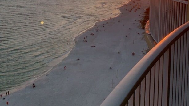 Une plage avec vue sur le coucher de soleil, un balcon avec une balustrade et une rangée de chaises longues.