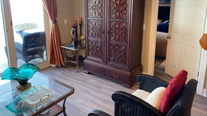 Une pièce avec une table à plateau en verre, des chaises en osier, un buffet en bois foncé et une porte donnant sur une autre pièce.
