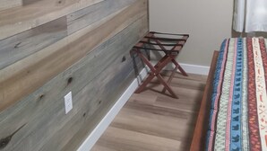 Une pièce avec un lambris en bois, un téléviseur fixé au mur, une petite étagère en bois et un lit recouvert d’une couverture colorée.