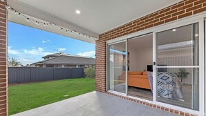 A covered patio with a sliding glass door leading to a living area with a sofa and a patterned rug.