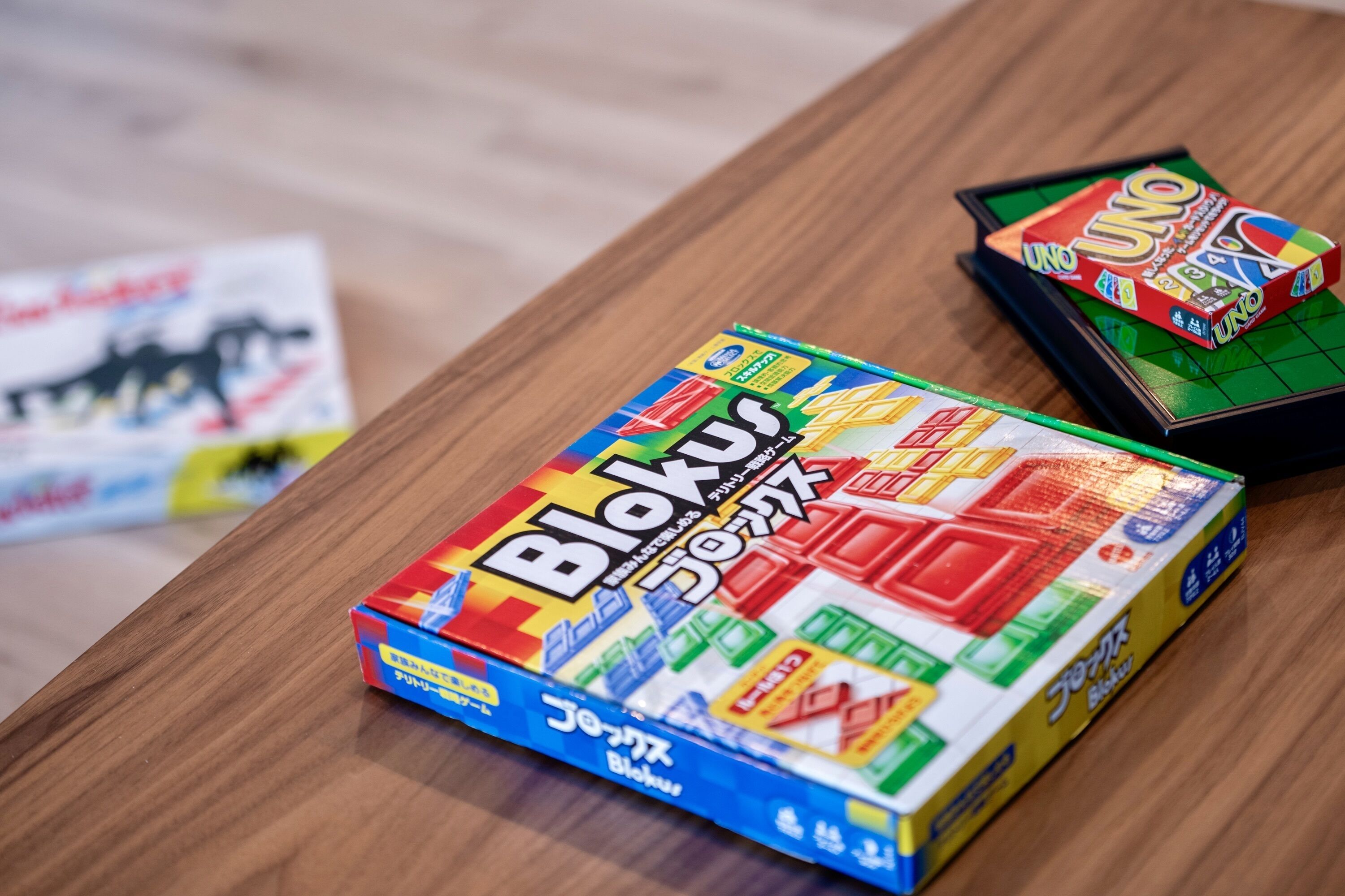 Et træbord med tre brætspil: Blokus, UNO, og et tredje spil med en hest på omslaget.