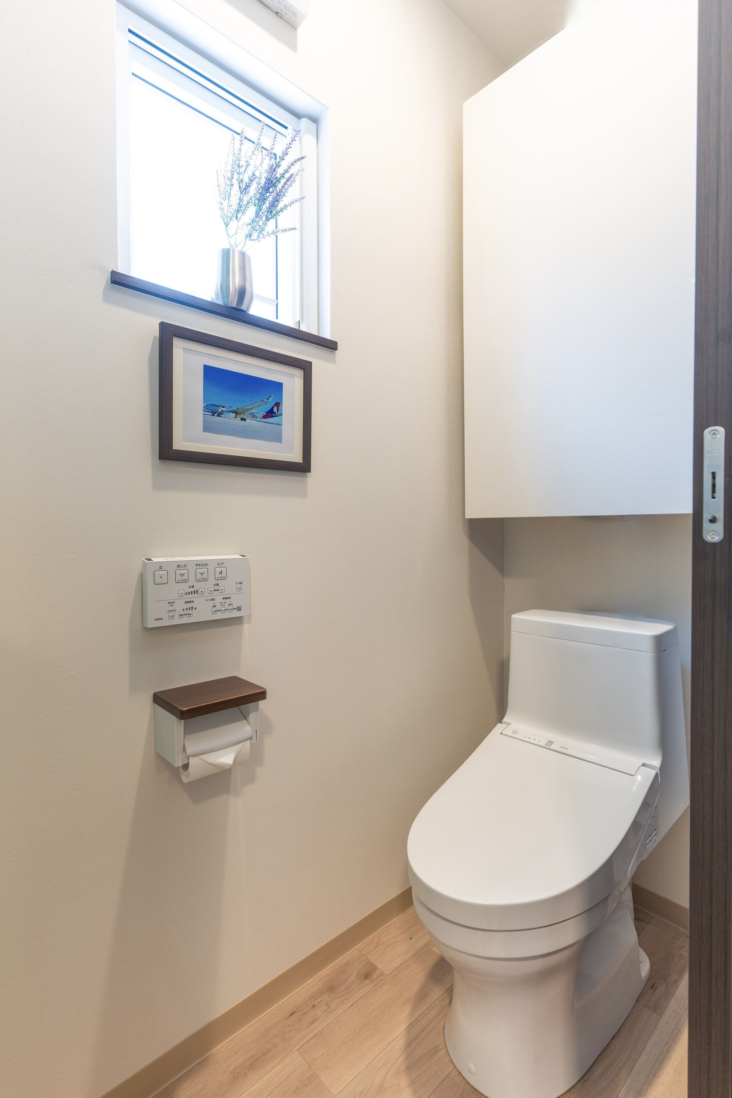 Un bagno moderno con il water, una finestra con un vaso e un quadro appeso al muro.