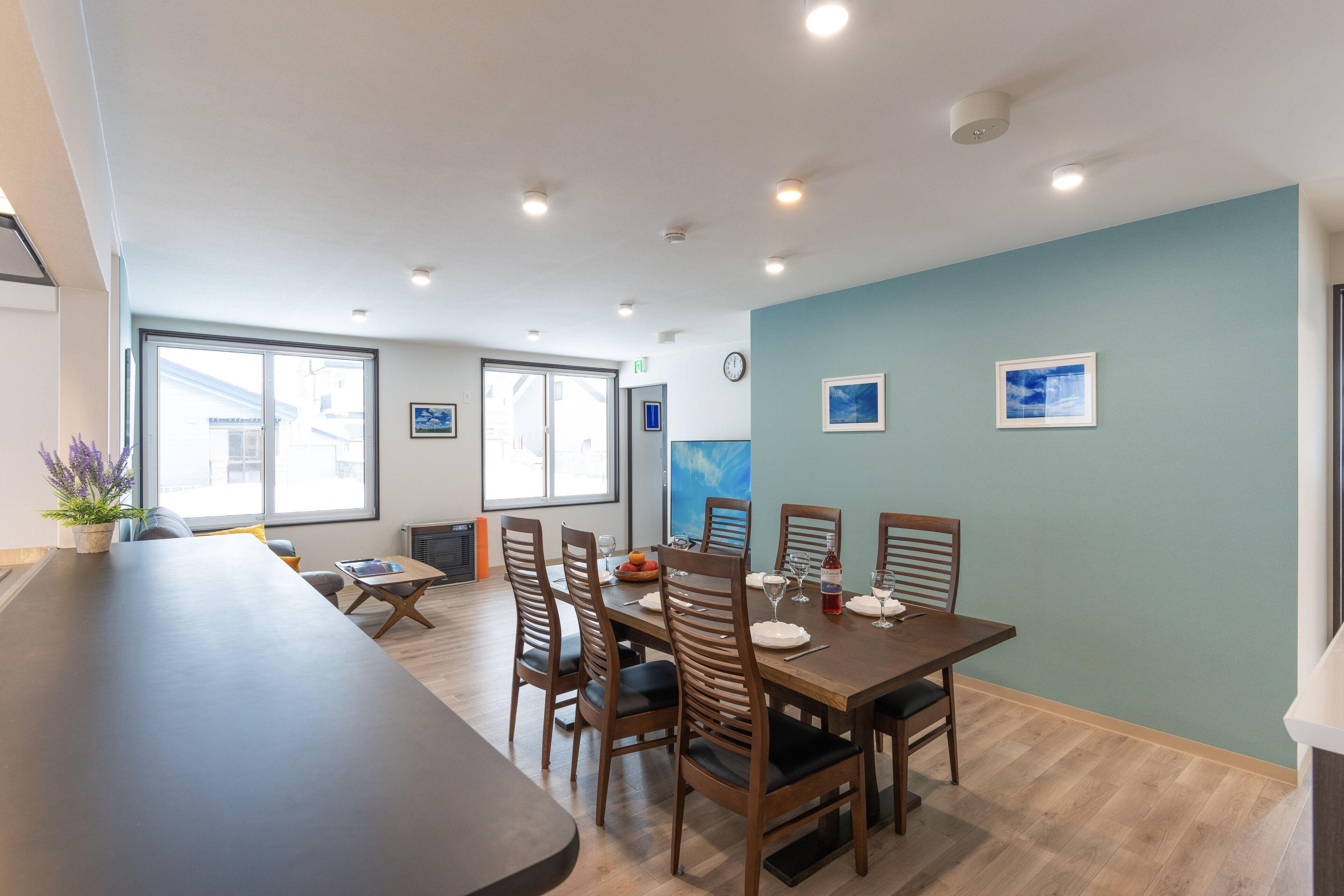 A dining area with a long table, chairs, and a small kitchen area in the background.
