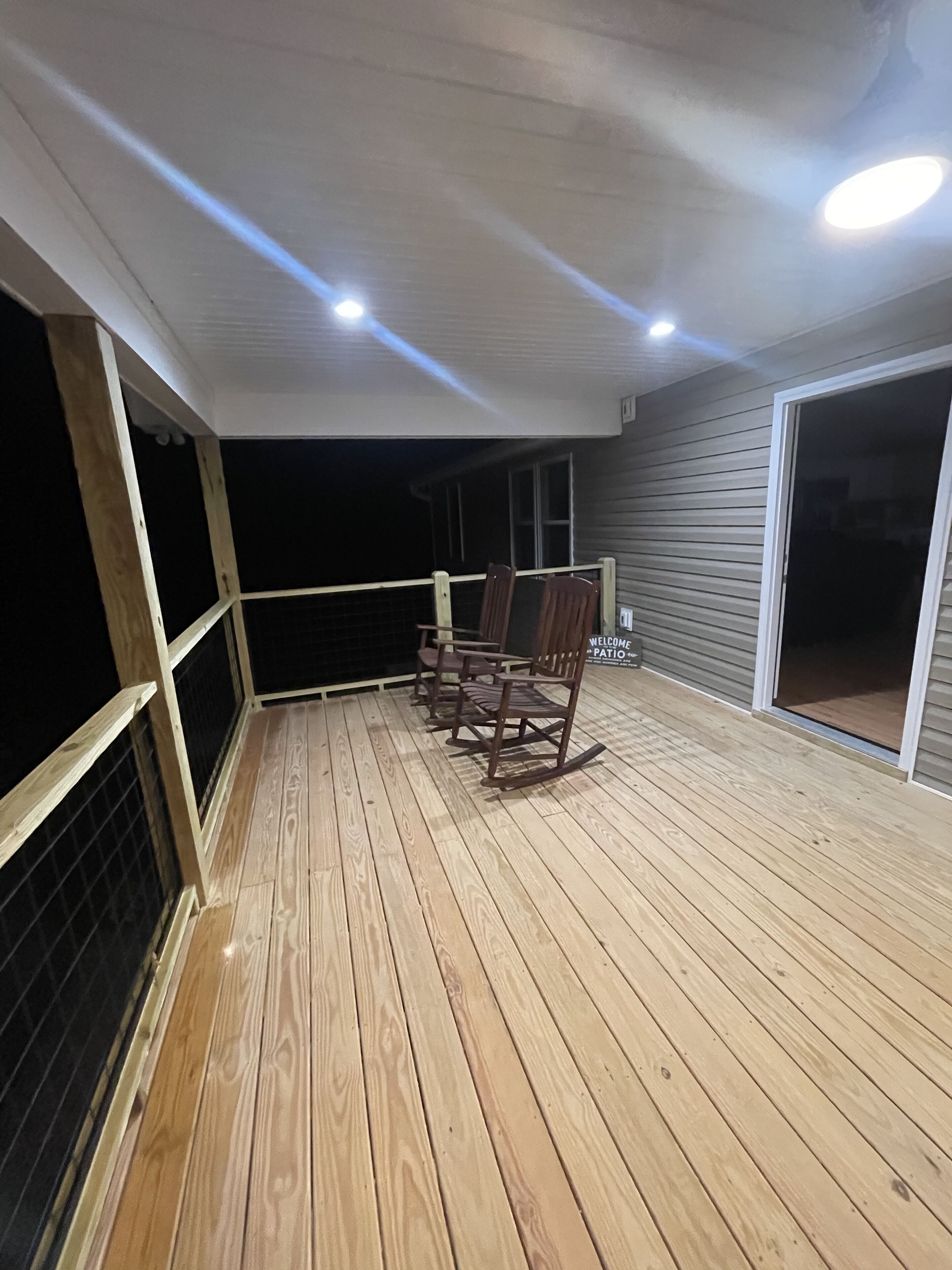 A wooden deck with a railing, a few wooden chairs, and a sign that reads "Welcome to the Patio."