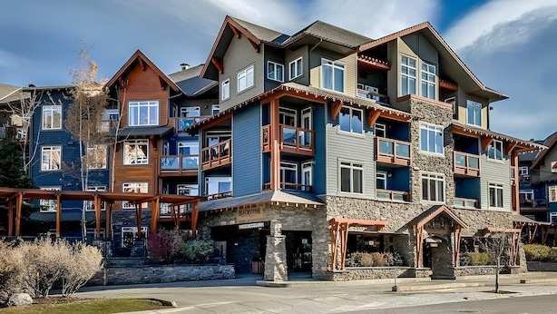 A multi-story hotel with balconies, stone facade, and a clear sky. - Top-Floor Condo with stunning mountain views! (Canmore)