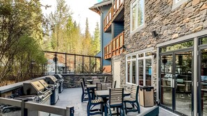 An outdoor patio with a stone wall, wooden deck, and a grill area. - Top-Floor Condo with stunning mountain views! (Canmore)