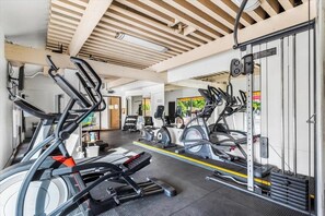Une salle de sport équipée de divers appareils d’exercice, notamment des tapis de course et des vélos d’appartement, sous un plafond en bois agrémenté de lucarnes.