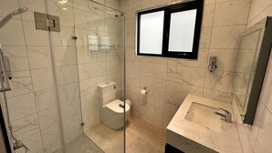 Un baño moderno con ducha acristalada, inodoro y lavabo con espejo.