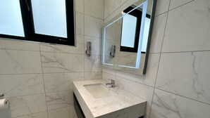 Un baño moderno con lavamanos de mármol, un espejo grande y una ventana.