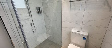 A modern bathroom with a glass-enclosed shower, a toilet, and a towel rack.