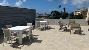 An outdoor patio with a table and chairs, a tiled floor, and a view of buildings and palm trees in the background.
