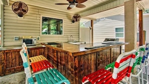 Una cocina con una isla de madera, microondas y lavamanos. Hay sillas coloridas y un ventilador de techo.