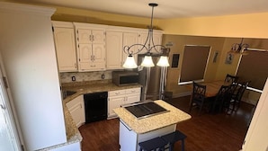 Una cocina con armarios blancos, encimera de granito, estufa integrada y un comedor con mesa y sillas de madera.