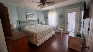 Un dormitorio con cama, ventilador de techo, una silla, cómoda y puerta.