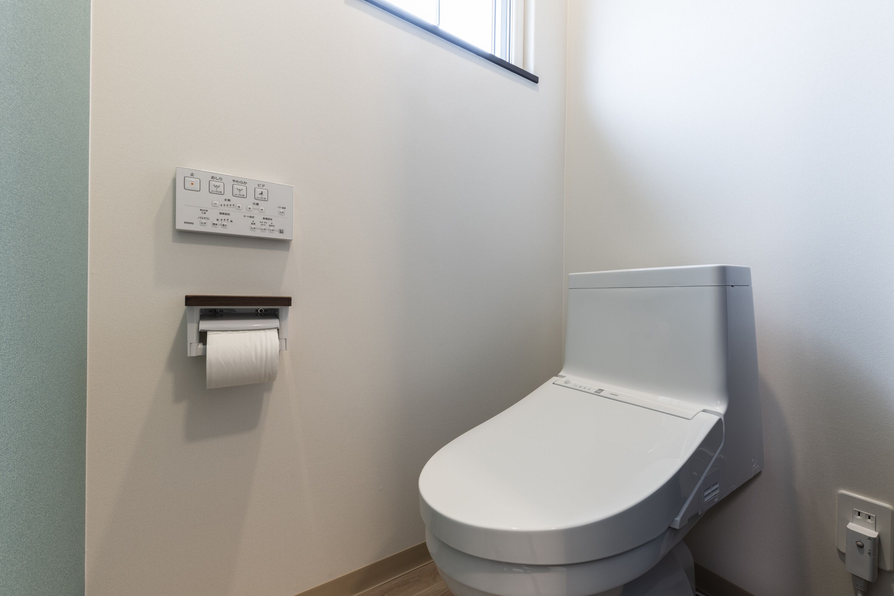 A modern bathroom with a toilet, a paper towel dispenser, and a wall-mounted control panel.