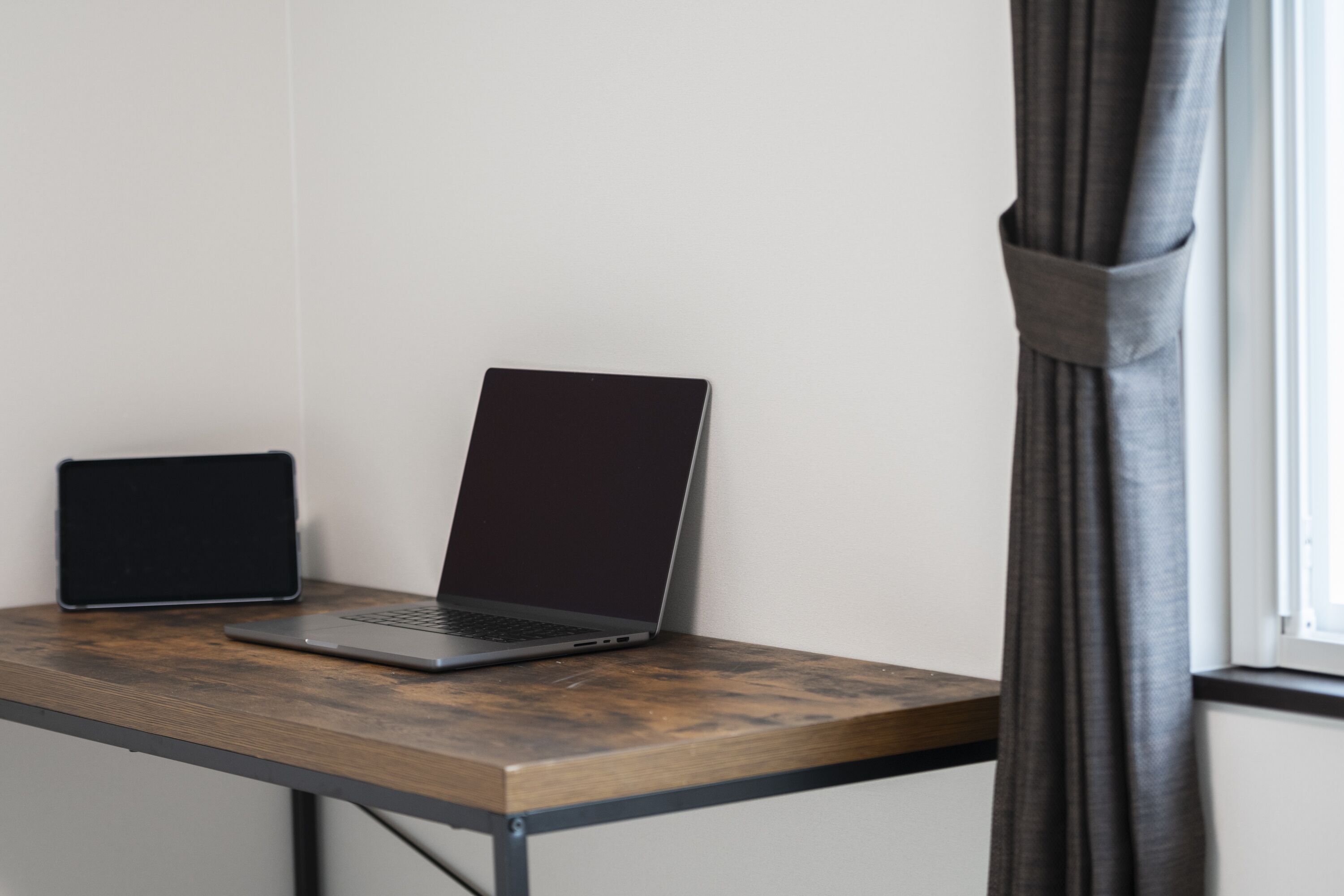 Un ordinateur portable est posé sur une table en bois, avec une fenêtre et des rideaux en arrière-plan.