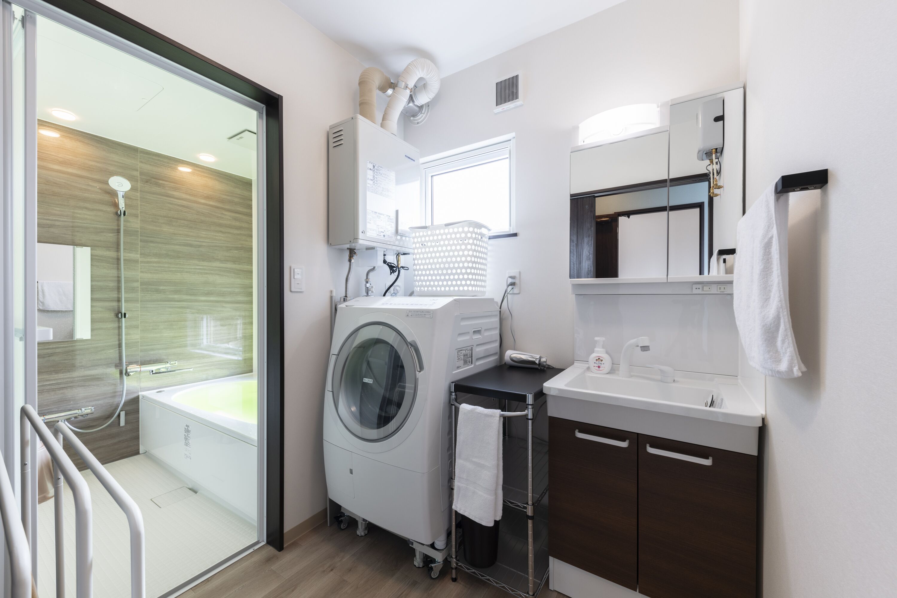 A modern bathroom with a glass shower enclosure, a built-in washing machine, a sink, and a mirror.