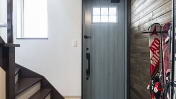 A modern interior with a wooden staircase, a door with a window, and skis leaning against a wall.