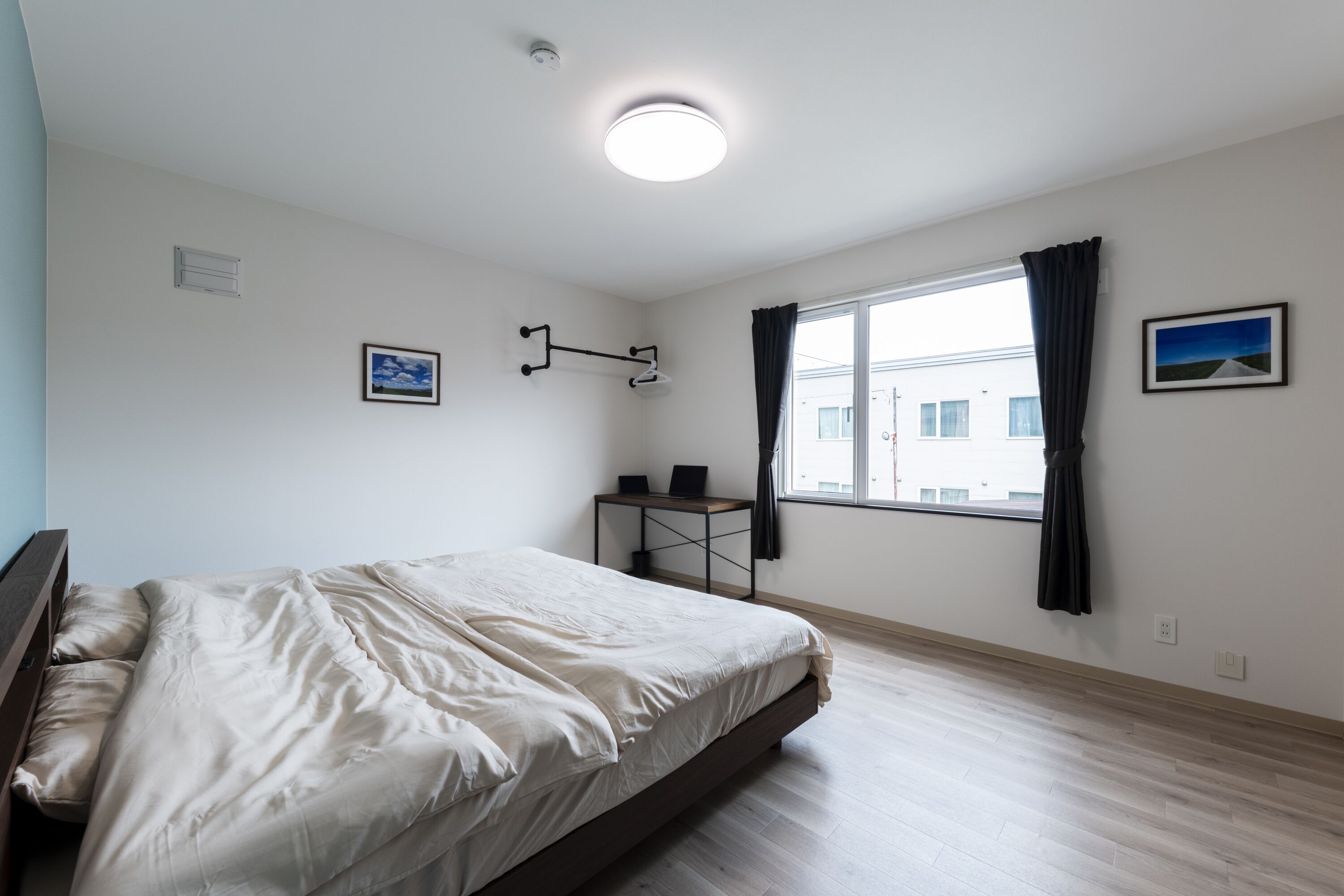 Ett sovrum med en säng, ett fönster med gardiner, ett litet bord med en lampa och en tavla på väggen.