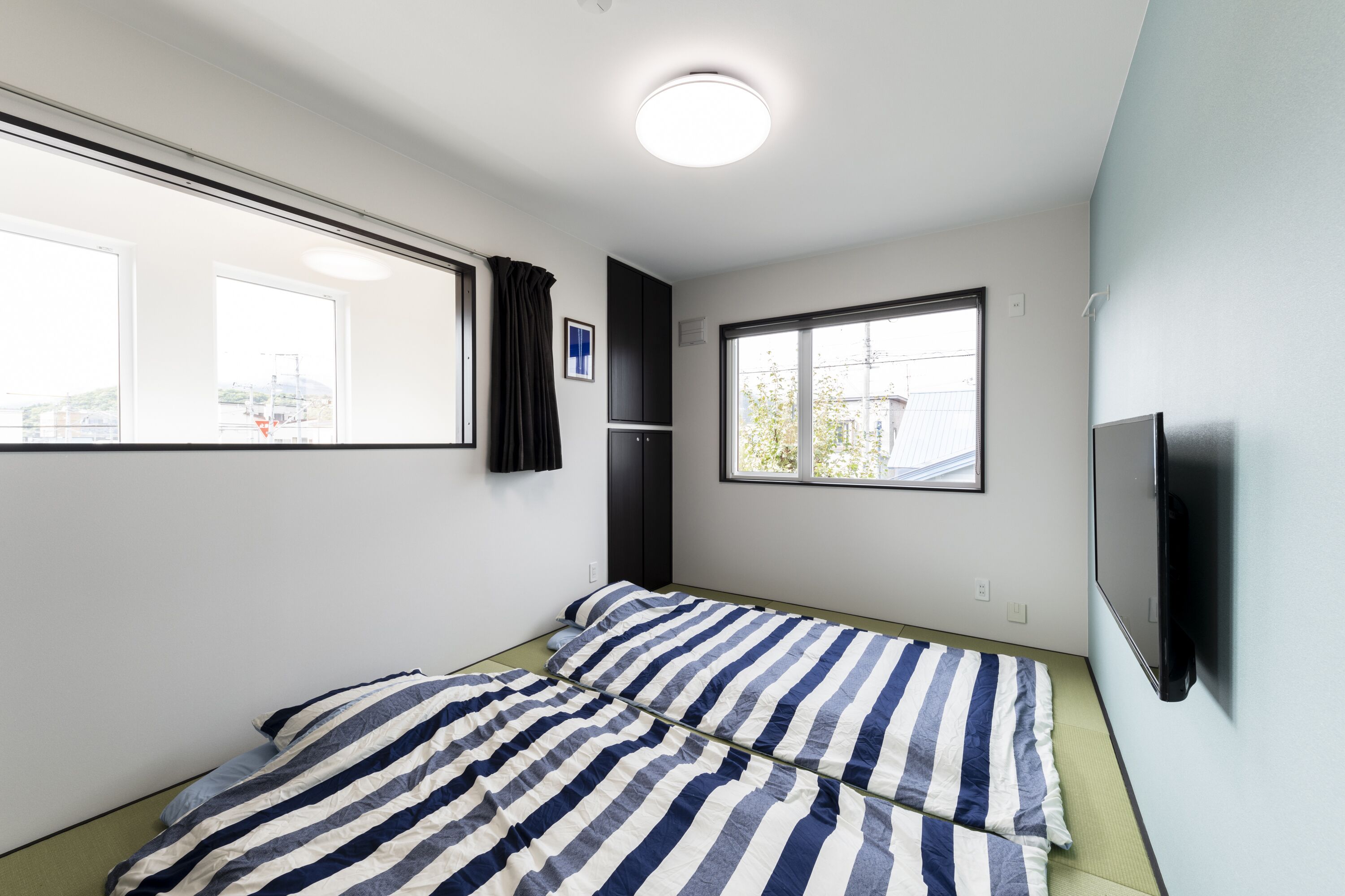 Ein kleines, modernes Schlafzimmer mit Bett, Fernseher und einem Fenster mit Vorhängen.