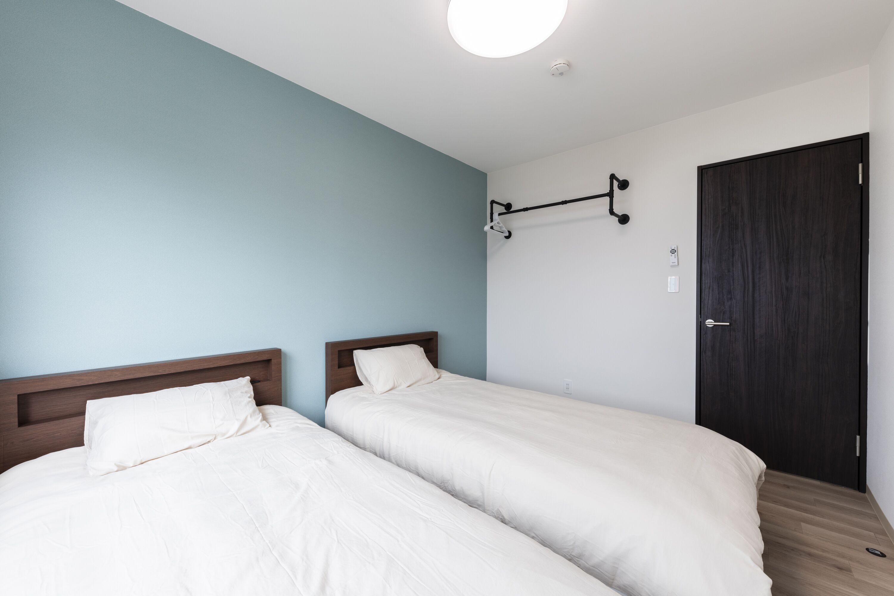 Una habitación con dos camas, cabecero de madera, lámpara de pared y una puerta oscura.