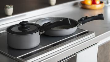 A kitchen with a modern induction cooktop, a kettle, and a frying pan on it.