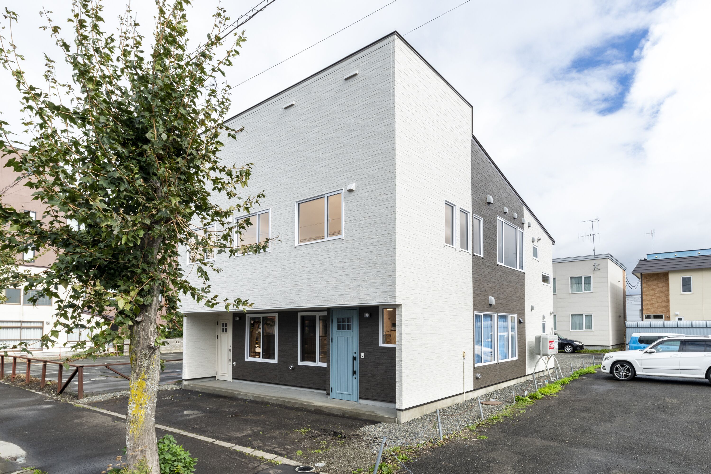 A modern two-story residential building with a light grey exterior, a blue door, and a small porch area.