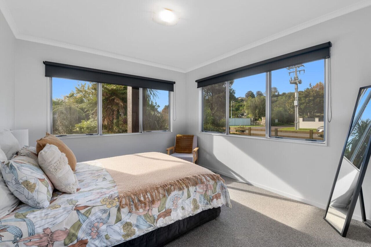 A bedroom with a bed, a chair, and large windows with blinds.